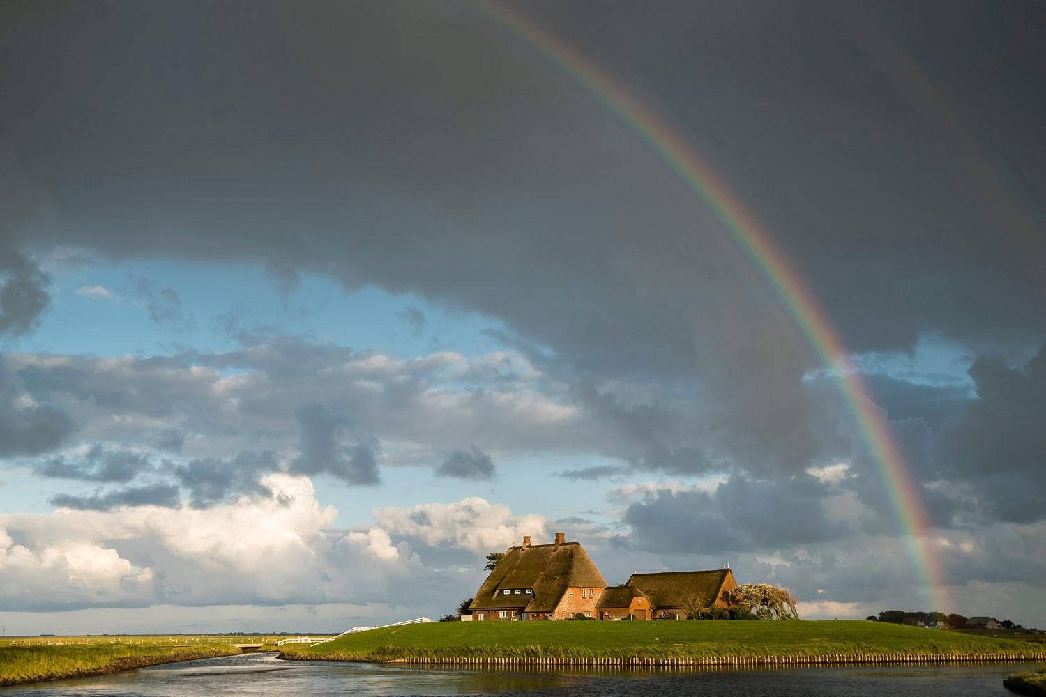 Haus auf einem Hügel, von Wasser umgeben - unter einem Regenbogen.