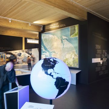 Globus mit Zugvogelrouten vor dem Luftbild des cuxhavener Watts