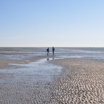 Zwei Menschen stehen auf einer weiten Wattfläche