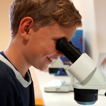Junge am Mikroskop der lächelt
